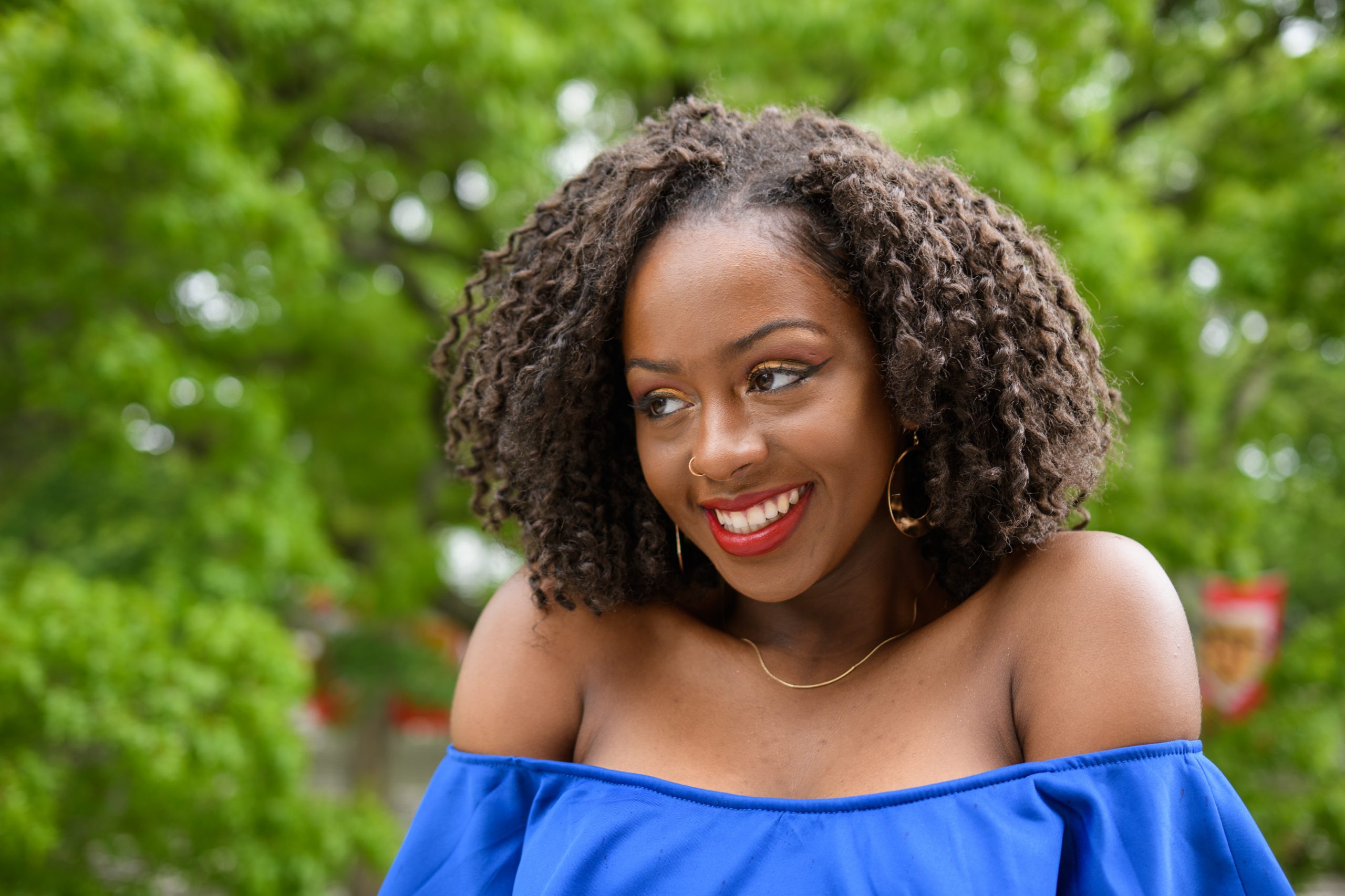 brown skin black woman with curly hair, red lipstick, black eyeliner, and strapless blue dres